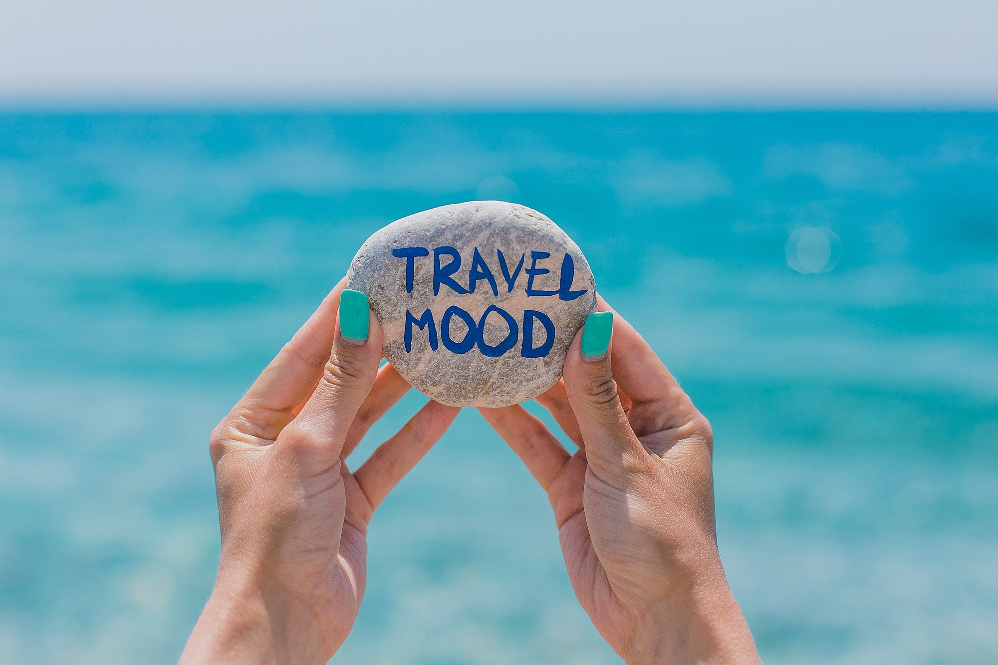 A young woman holds a stone with the inscription "Travel mood" in her hands